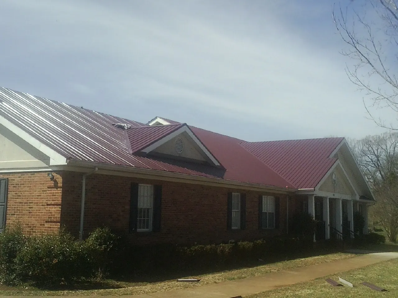 Red metal roof with gabled entries on a long brick building, from a Hail Damage Roof Repair job in Fairbanks