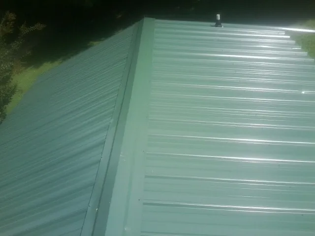 New green metal panels meeting at the ridge of a roof — Flat Roof Repair work by our crew in Fairbanks