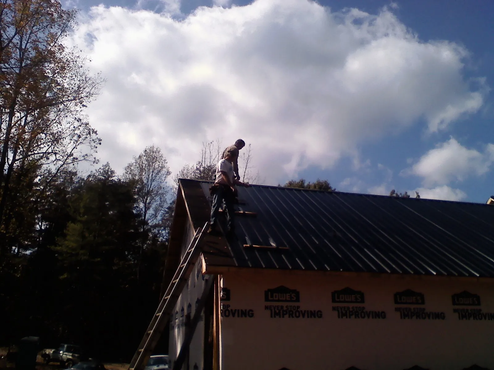 Roofer fastening dark metal panels high against a cloudy sky, from a Roof Inspection job in Fairbanks