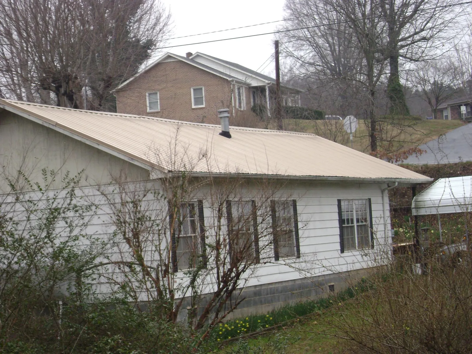 Tan metal roof on a white sided house set into a hillside — Commercial Roofing by Roofing Brothers in Fairbanks
