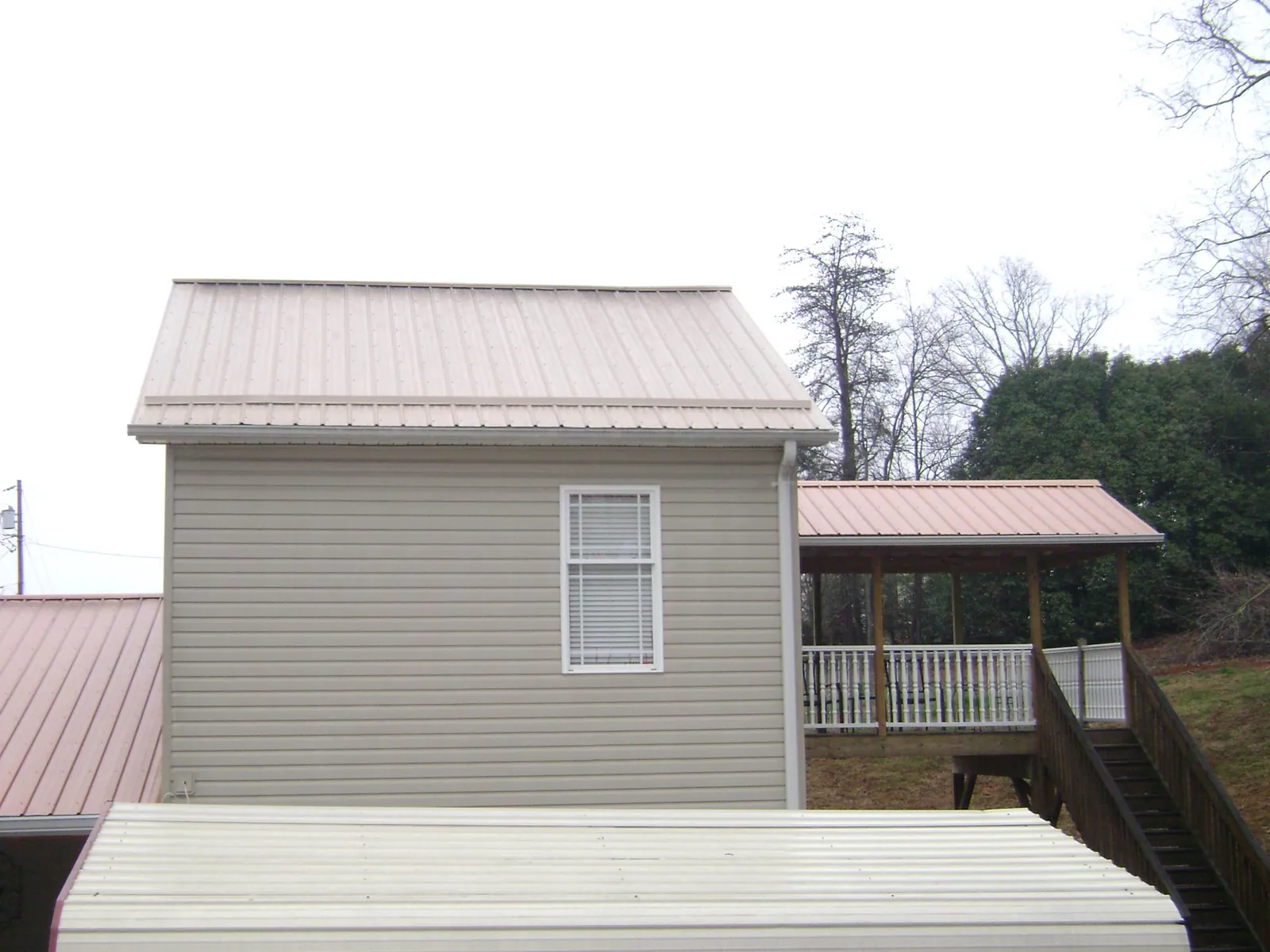 Tan metal roofs on a two story addition and attached porch, from a Roof Replacement job in Fairbanks