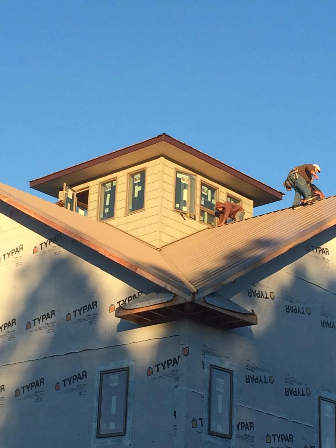 Roofers working around a rooftop cupola on a new metal roof at sunset — Roof Waterproofing in Fairbanks by Roofing Brothers